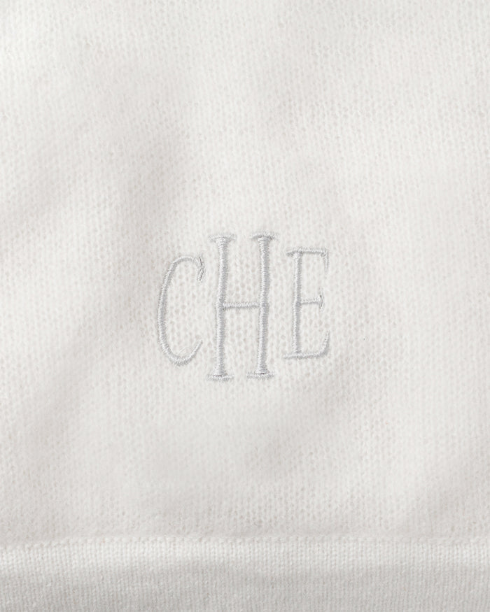 Close-up of Petite Plumes ivory Cashmere Baby Blanket, handmade with CHE embroidered in the center. The soft, slightly fuzzy texture makes it an ideal luxury gift for babies.