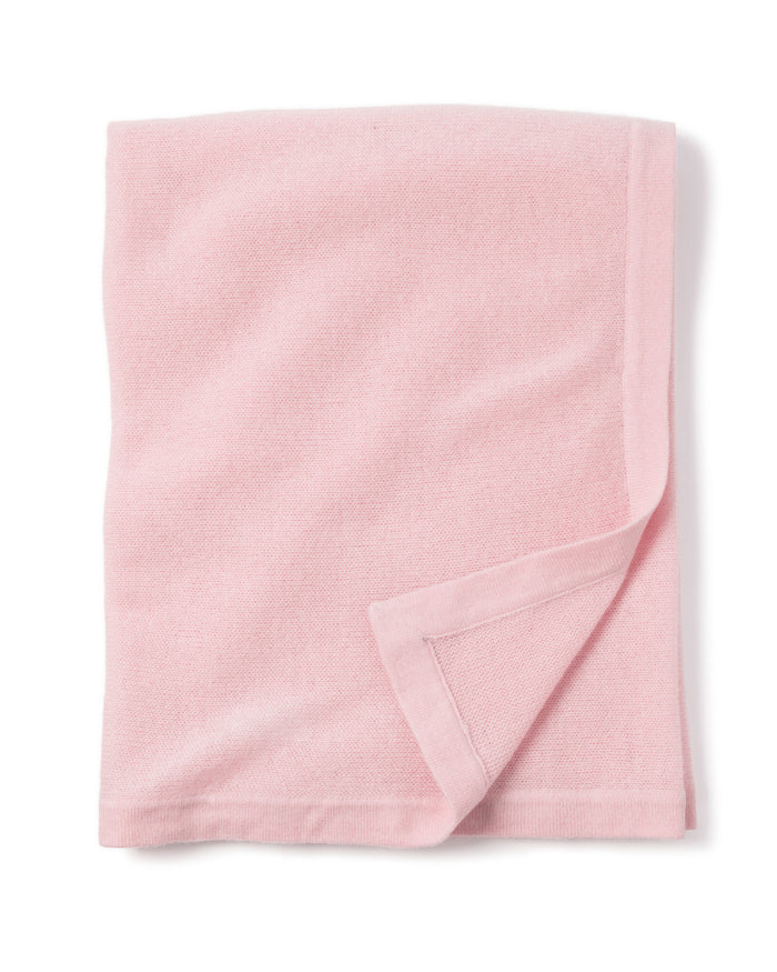 A soft, cashmere baby blanket in rose from Petite Plume is neatly folded against a white background, featuring a simple border detail. Handmade in Nepal, it makes the perfect luxury baby gift.
