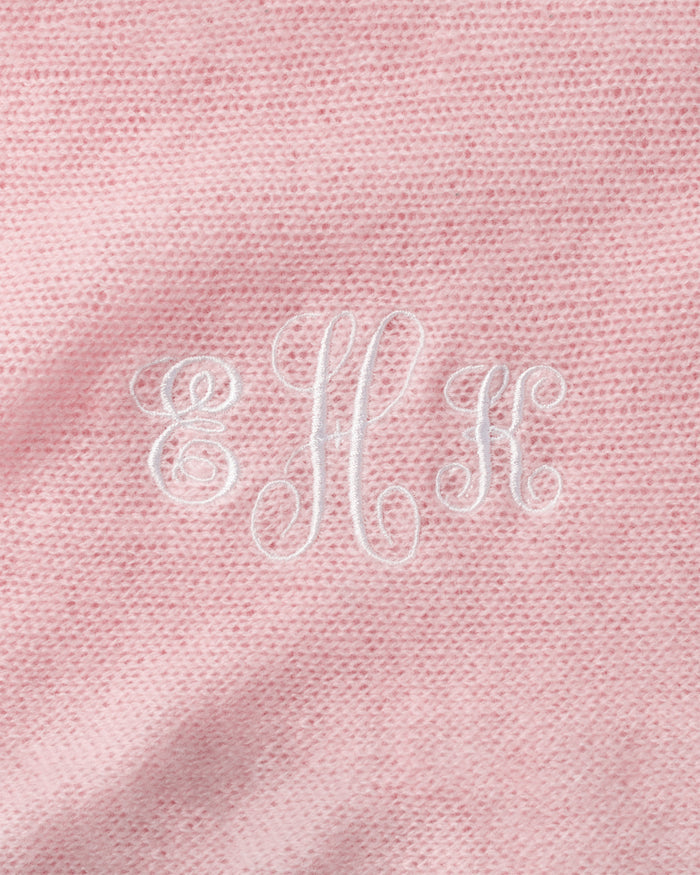 The Petite Plume Cashmere Baby Blanket in Rose features pink fabric with embroidered white EHK letters in ornate script. Handmade in Nepal, this luxury gift boasts a subtly textured appearance, epitomizing elegance and warmth.