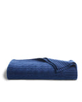 The Cashmere Cable Knit Throw in Navy by Petite Plume is neatly folded on a white background, showcasing its textured pattern and partially revealing the underside. This exquisite cashmere-wool throw adds elegance to any home decor.