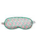 A pure silk sleep mask from Petite Plume features a vibrant arch pattern in pink and green with CB initials, a matching green border, and complements the charm of their pajamas. It includes a small tag reading PETITE.