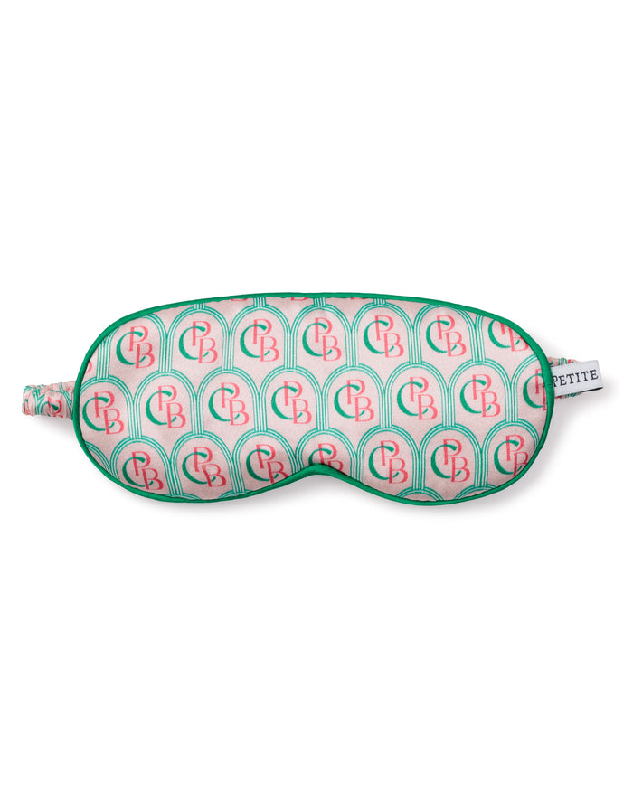 A pure silk sleep mask from Petite Plume features a vibrant arch pattern in pink and green with CB initials, a matching green border, and complements the charm of their pajamas. It includes a small tag reading PETITE.