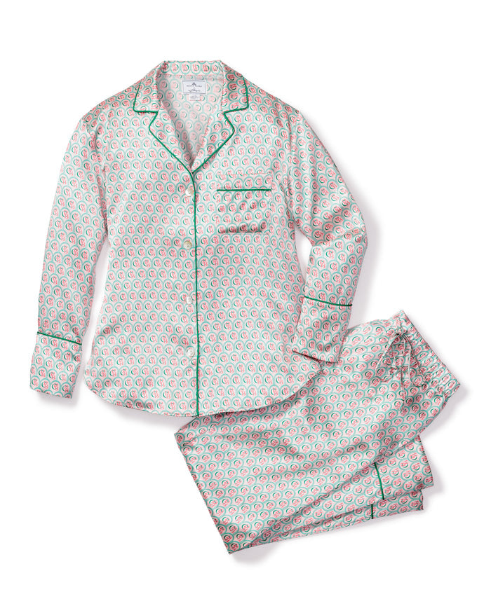 Indulge in the luxury of the Colony Hotel x Petite Plume Womens Silk Pajama Set, featuring a white base with red and green floral patterns. The long-sleeved top has a collar, buttons, and green piping, while the pants provide a relaxed fit for ultimate comfort.