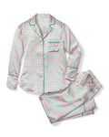 Indulge in the luxury of the Colony Hotel x Petite Plume Womens Silk Pajama Set, featuring a white base with red and green floral patterns. The long-sleeved top has a collar, buttons, and green piping, while the pants provide a relaxed fit for ultimate comfort.