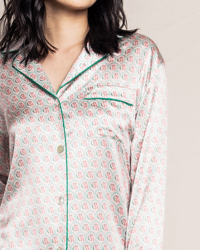 The woman is wearing the cream Petite Plume Womens Silk Pajama Top from the exclusive Colony Hotel collection, showcasing a charming pink and red pattern with green piping. The image shows her from the neck down, with hair softly falling on her shoulders.
