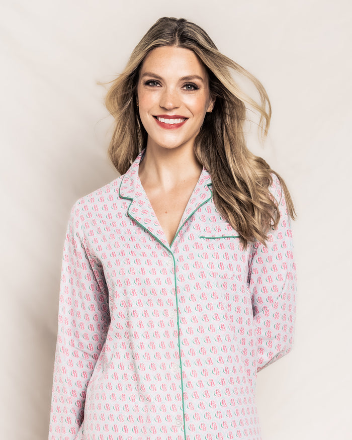 A smiling woman with long blonde hair wears a Colony Hotel x Petite Plume Womens Exclusive Print Pajama Set by Petite Plume. She stands against a light background, slightly tilting her head, with her hair gently flowing to the side.