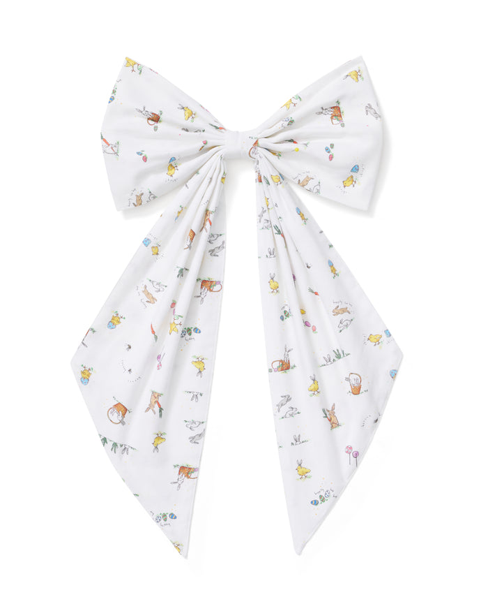 An Easter Basket and Wreath Bow in Easter Frolic with a large white bow featuring a pastel floral pattern is tied at the bottom of a wreath made of small white and pink flowers, hanging on a beige door.