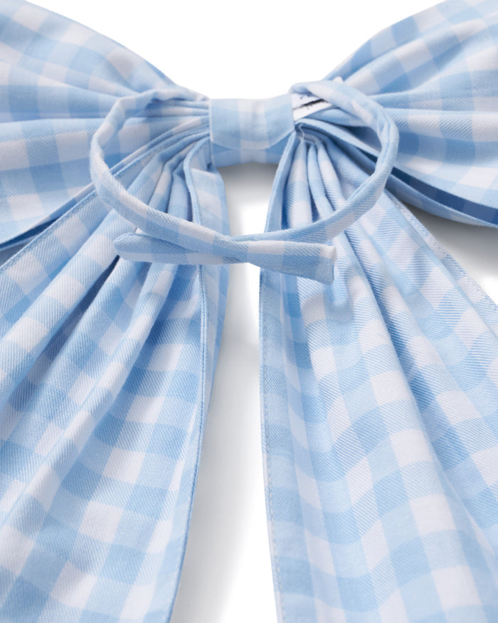A floral wreath of small white and pink blooms hangs on a beige door, adorned with the Easter Basket and Wreath Bow in Light Blue Gingham featuring long ribbon tails.