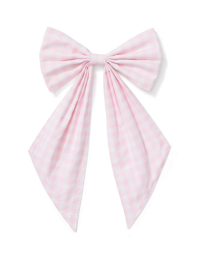 A spring wreath adorned with small white and pink flowers and greenery hangs on a beige door, finished with the Easter Basket and Wreath Bow in Pink Gingham at the bottom.