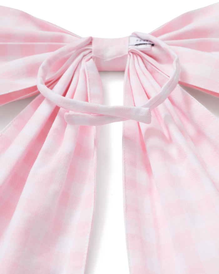 A spring wreath adorned with small white and pink flowers and greenery hangs on a beige door, finished with the Easter Basket and Wreath Bow in Pink Gingham at the bottom.