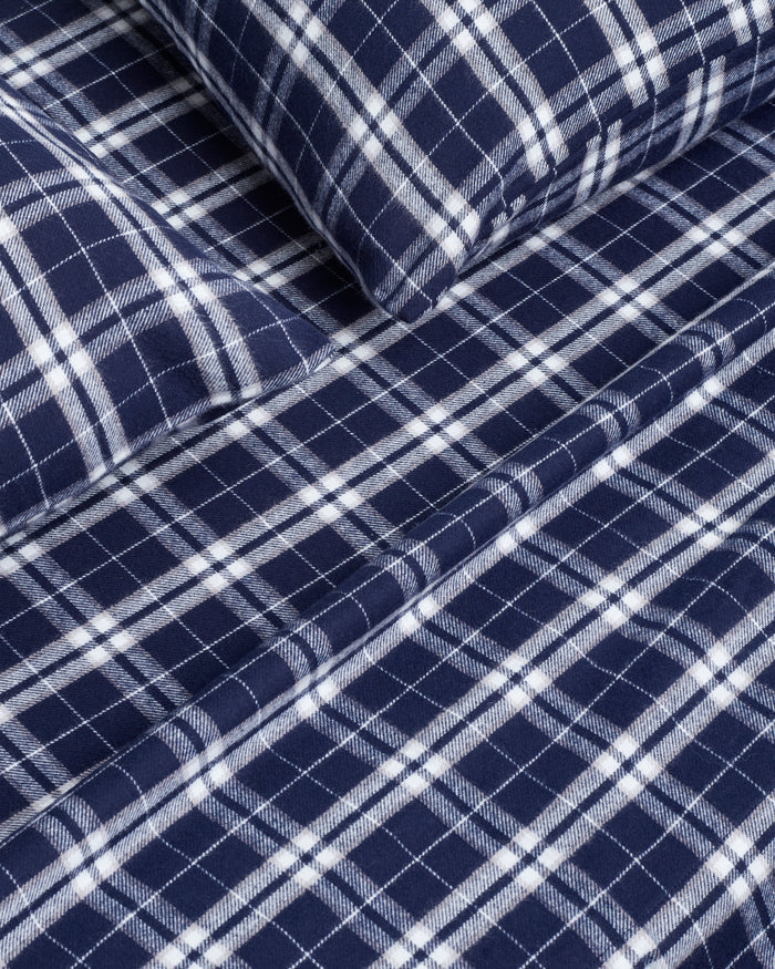 The Flannel Bed Sheet Set in Oxford Tartan features neatly folded navy blue and white plaid sheets with matching pillowcases, displayed on a white background.