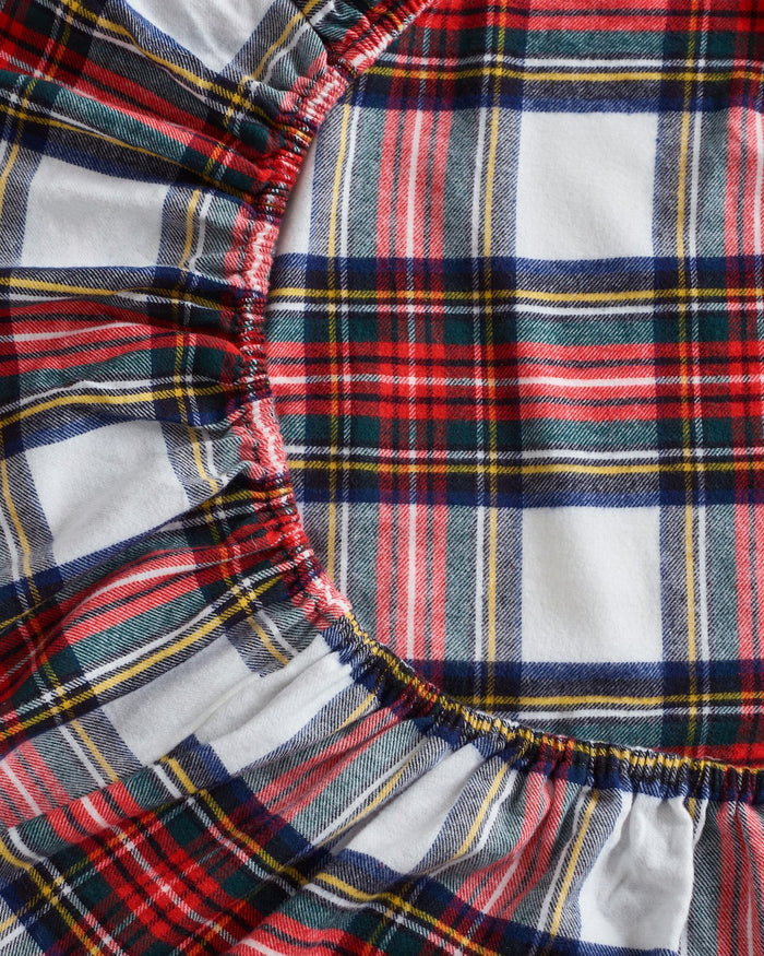 Close-up of Petite Plumes Flannel Crib Sheet in Balmoral Tartan showcasing a vibrant plaid design with red, white, blue, green, and yellow stripes. The circular gathered pattern creates a ruffled texture similar to a cozy cotton flannel sheet set.