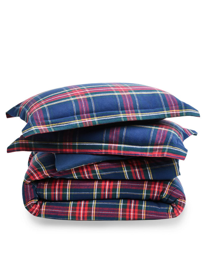 The Petite Plume Flannel Duvet Set in Windsor Tartan, featuring a blue, red, and yellow plaid pattern, is neatly folded. Made of brushed cotton flannel, the duvet and stacked pillows showcase a classic tartan design for cozy nights.