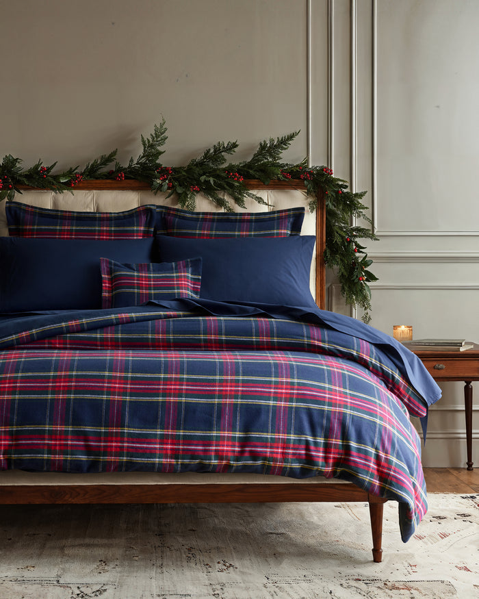 The Petite Plume Flannel Duvet Set in Windsor Tartan, featuring a blue, red, and yellow plaid pattern, is neatly folded. Made of brushed cotton flannel, the duvet and stacked pillows showcase a classic tartan design for cozy nights.