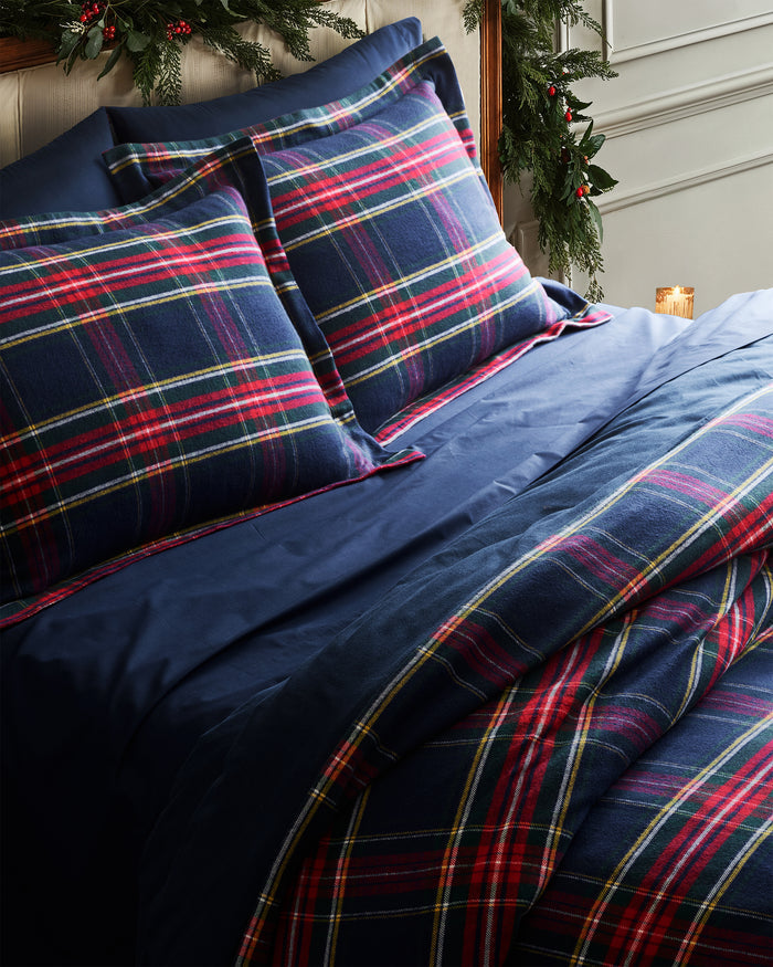 The Petite Plume Flannel Duvet Set in Windsor Tartan, featuring a blue, red, and yellow plaid pattern, is neatly folded. Made of brushed cotton flannel, the duvet and stacked pillows showcase a classic tartan design for cozy nights.