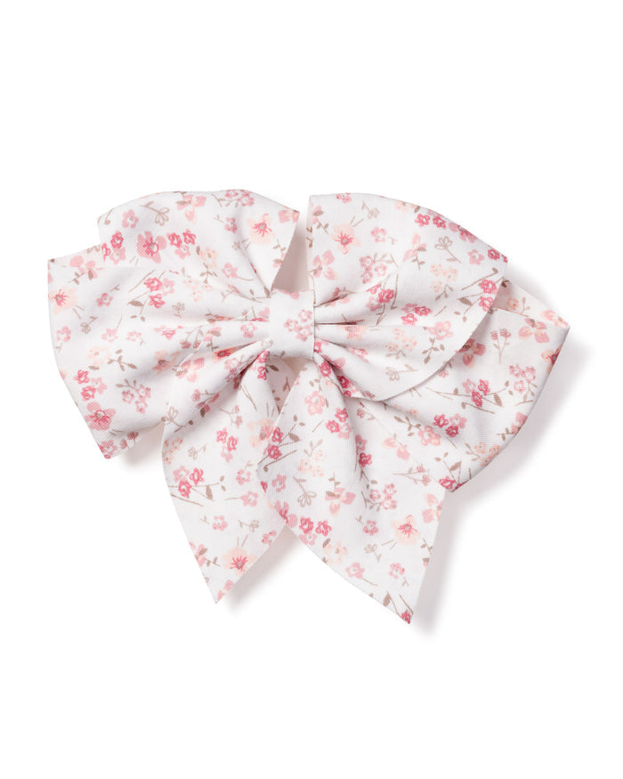 The Petite Plume Girls Dorset Floral Hair Bow features a white fabric with small pink flowers and delicate gray leaves, tied in symmetrical loops and tails. Ideal as a holiday gift or charming stocking stuffer.