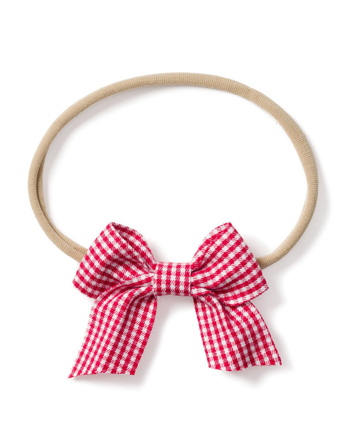 The Petite Plume Girls Hair Bow in Red Mini Gingham is a beige elastic headband with a delightful red and white checkered bow at the bottom, perfect for pajamas and an adorable choice for girls.