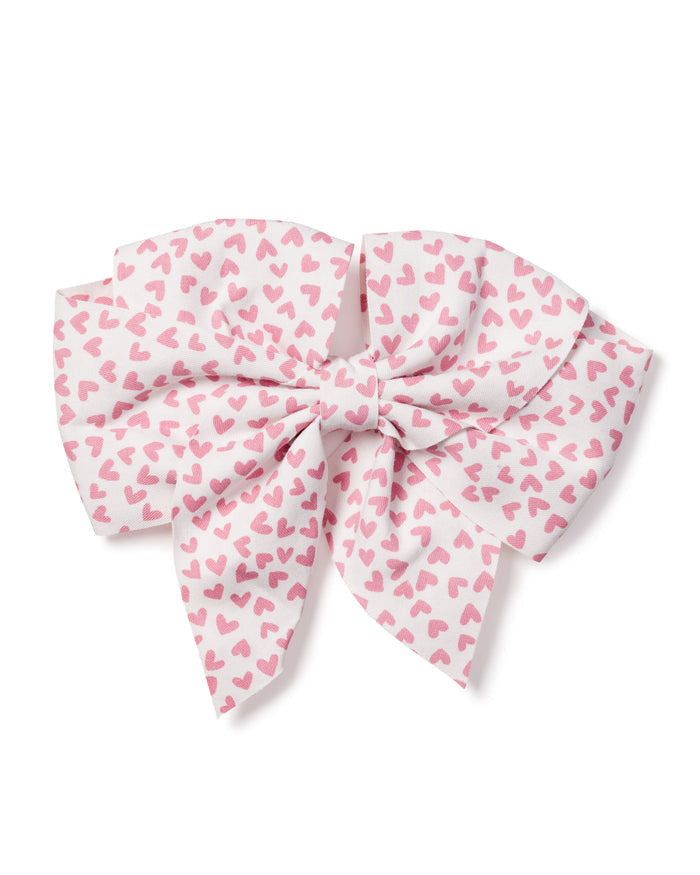 The Petite Plume Girls Hair Bow in Sweethearts is a large fabric bow adorned with a pattern of small pink hearts on white. Neatly tied with layered loops and tails, it offers a fluffy look, making it an ideal festive accessory or charming holiday gift for girls.