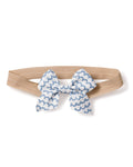 A charming beige elastic headband, adorned with Petite Plumes Girls Hair Bows in La Mer, features a white and blue scalloped wave pattern bow, making it an ideal stylish accessory for girls.