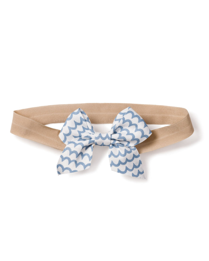 A charming beige elastic headband, adorned with Petite Plumes Girls Hair Bows in La Mer, features a white and blue scalloped wave pattern bow, making it an ideal stylish accessory for girls.