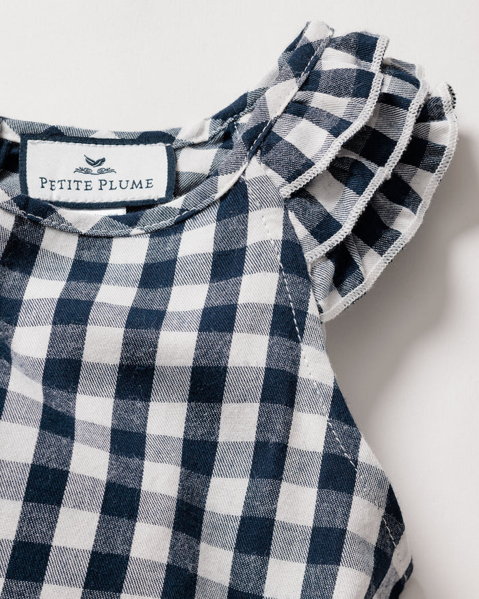 Close-up of a navy gingham print dress with ruffled sleeves. This lightweight twill nightgown has a fabric label at the neckline with Petite Plume and a small bird illustration, featuring a soft, textured appearance.
