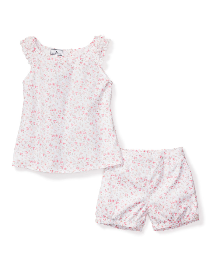 The Girls Twill Amelie Short Set in Dorset Floral by Petite Plume is a cotton pajama set with a sleeveless top and shorts, featuring white fabric adorned with delicate pink flower buds and ruffled shoulder accents for a feminine touch.