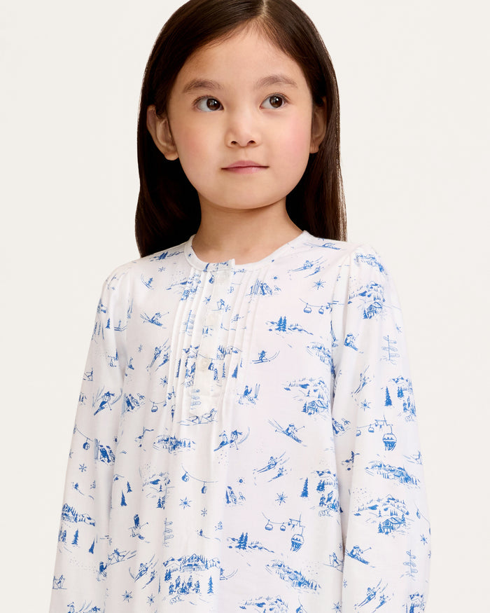 The Girl's Twill Beatrice Nightgown in Chalet Toile features long sleeves, knee-length, white fabric with blue scenic prints, a round neckline, pintucks on the chest, a loose fit, and button details at the neck.