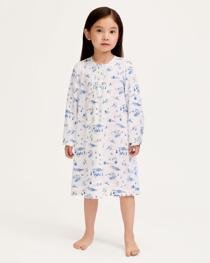 The Girl's Twill Beatrice Nightgown in Chalet Toile features long sleeves, knee-length, white fabric with blue scenic prints, a round neckline, pintucks on the chest, a loose fit, and button details at the neck.