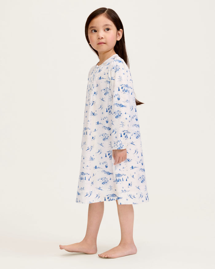 The Girl's Twill Beatrice Nightgown in Chalet Toile features long sleeves, knee-length, white fabric with blue scenic prints, a round neckline, pintucks on the chest, a loose fit, and button details at the neck.
