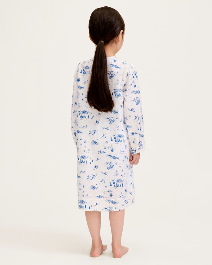 The Girl's Twill Beatrice Nightgown in Chalet Toile features long sleeves, knee-length, white fabric with blue scenic prints, a round neckline, pintucks on the chest, a loose fit, and button details at the neck.