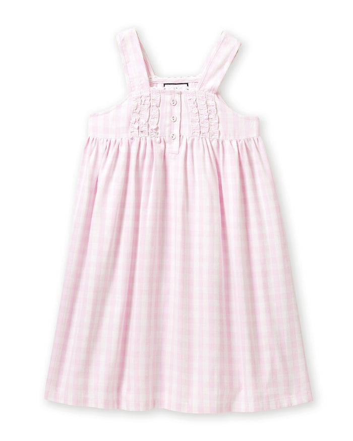 Four individuals in light-colored sleepwear pose on a stone wall in a sunny, wooded area. Two sit relaxed, and two stand below. One wears the Petite Plume Girls Twill Charlotte Nightgown in Pink Gingham, highlighting the natural and comforting setting of their attire.