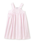 Four individuals in light-colored sleepwear pose on a stone wall in a sunny, wooded area. Two sit relaxed, and two stand below. One wears the Petite Plume Girls Twill Charlotte Nightgown in Pink Gingham, highlighting the natural and comforting setting of their attire.