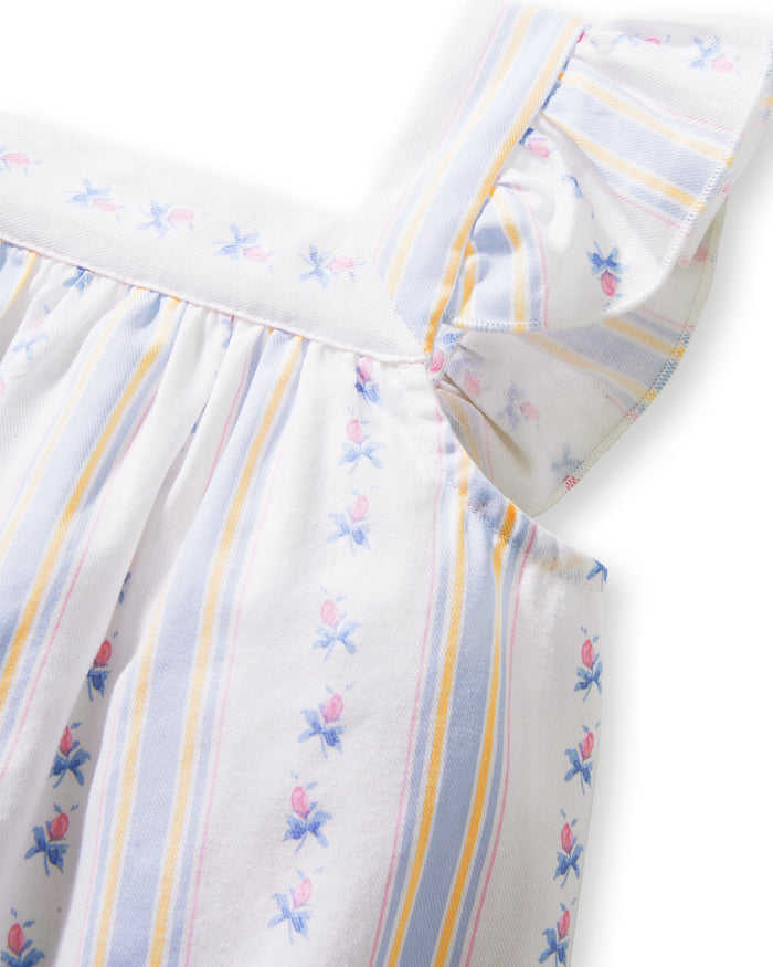 A young girl with curly hair smiles barefoot, wearing the Girl's Twill Clara Short Set in Cottage Stripe— a white sleeveless nightgown and matching shorts—against a plain, light background.