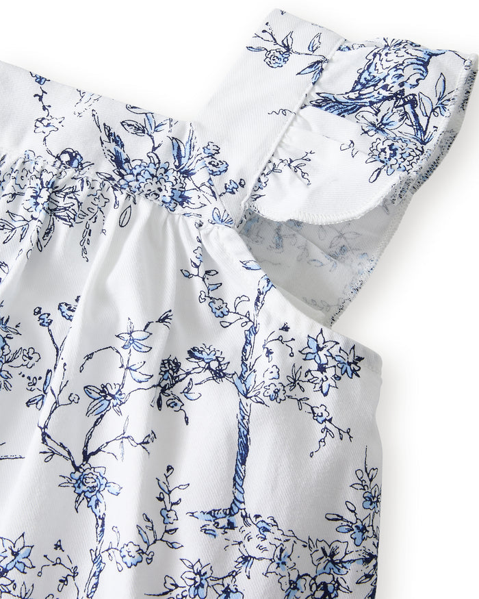 A young girl with long brown hair stands barefoot, smiling in the Girl's Twill Clara Short Set in Timeless Toile—a white top and matching blue floral shorts—posing against a plain light background.