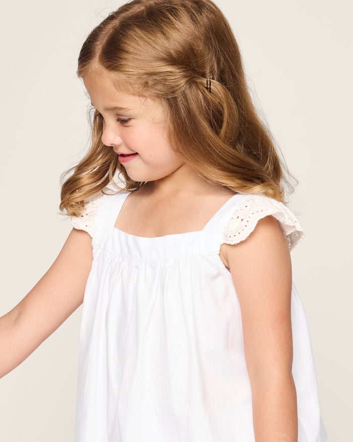 A young girl with light brown hair smiles while looking to the side, wearing Petite Plumes Girls Twill Clara Short Set in White. She is posed against a plain light background.