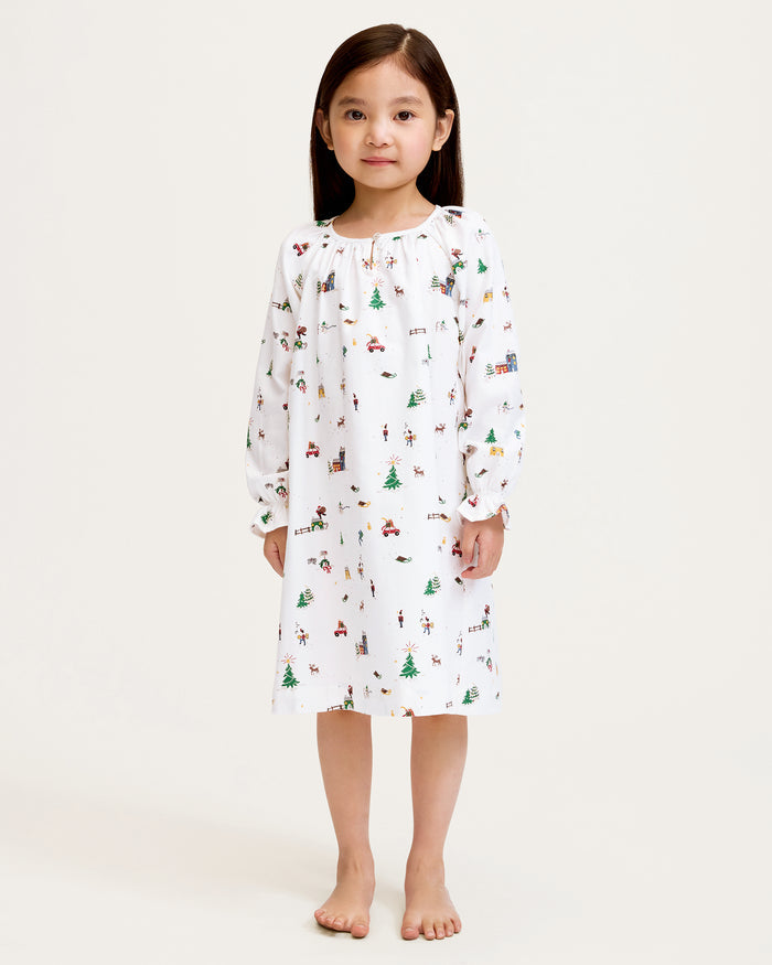The Girl's Twill Delphine Nightgown in Holiday Town is a white, long-sleeved children's nightgown with colorful festive prints and features ruffled cuffs and a gathered neckline.