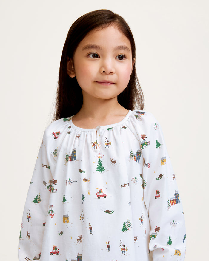 The Girl's Twill Delphine Nightgown in Holiday Town is a white, long-sleeved children's nightgown with colorful festive prints and features ruffled cuffs and a gathered neckline.