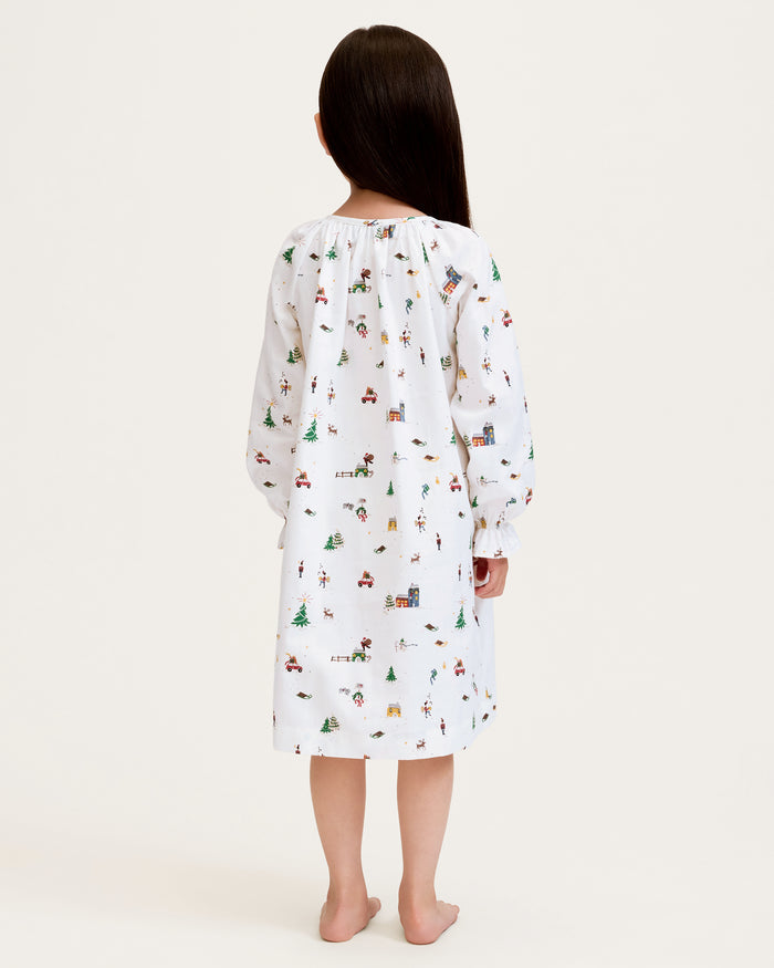 The Girl's Twill Delphine Nightgown in Holiday Town is a white, long-sleeved children's nightgown with colorful festive prints and features ruffled cuffs and a gathered neckline.