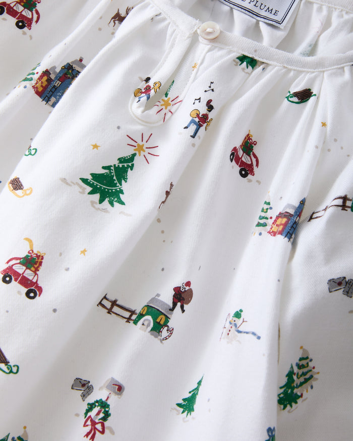 The Girl's Twill Delphine Nightgown in Holiday Town is a white, long-sleeved children's nightgown with colorful festive prints and features ruffled cuffs and a gathered neckline.