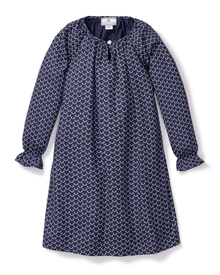 The Girls Twill Delphine Nightgown in Nordic Antlers by Petite Plume features long sleeves, a navy hue with a white scallop design, a round neckline, small front button closure, and gathered cuffs for comfort and style. Crafted from moisture-wicking twill.