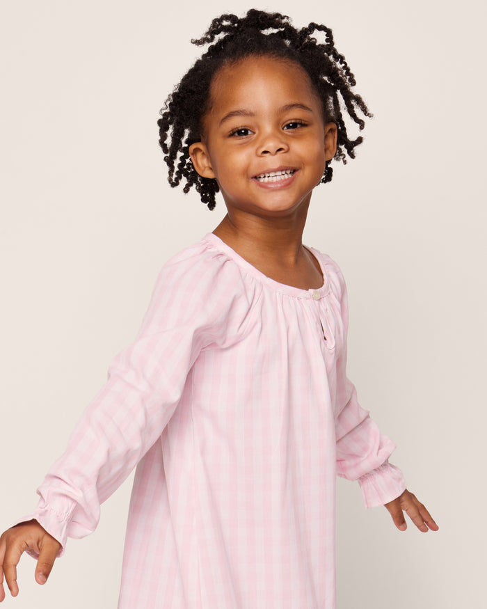 The Petite Plume Girls Twill Delphine Nightgown in Pink Gingham features long sleeves, a rounded neckline with a small keyhole opening, and ruffled cuffs, made from flame-retardant fabric.