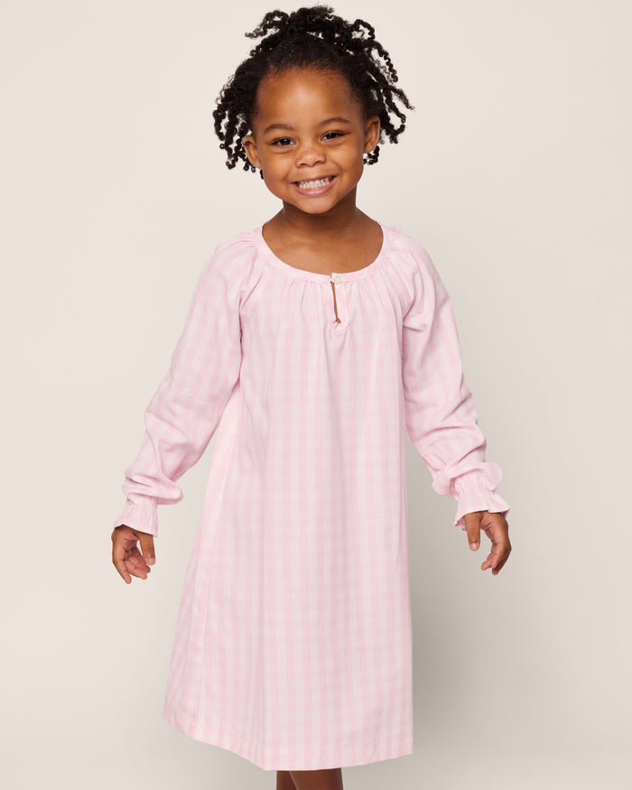 The Petite Plume Girls Twill Delphine Nightgown in Pink Gingham features long sleeves, a rounded neckline with a small keyhole opening, and ruffled cuffs, made from flame-retardant fabric.