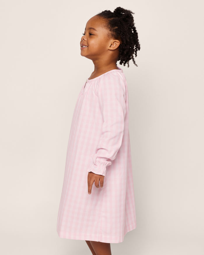 The Petite Plume Girls Twill Delphine Nightgown in Pink Gingham features long sleeves, a rounded neckline with a small keyhole opening, and ruffled cuffs, made from flame-retardant fabric.