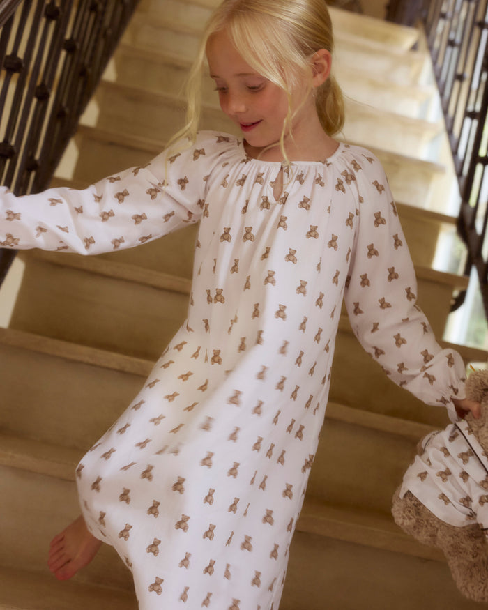 The Girl's Twill Delphine Nightgown in Teddy Tales features long sleeves, a white fabric with an all-over brown teddy bear print, a gathered neckline, ruffled cuffs, and a button closure at the collar.