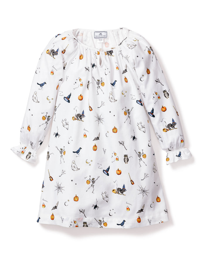 The Petite Plume Girls Twill Delphine Nightgown in Trick or Treat showcases Halloween-themed prints like pumpkins, ghosts, and bats. This white long-sleeve gown features gathered sleeves and a button-fastened neckline, ideal for the festive season.