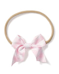 The Petite Plume Girls Twill Hair Bows in Pink Gingham is a soft, beige elastic headband featuring a large pink and white checkered bow, perfect for adding style and sophistication to girls hair.