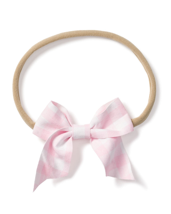 The Petite Plume Girls Twill Hair Bows in Pink Gingham is a soft, beige elastic headband featuring a large pink and white checkered bow, perfect for adding style and sophistication to girls hair.
