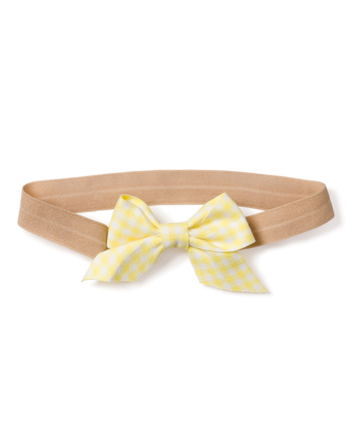 The Petite Plume Girls Twill Hair Bows in Yellow Gingham feature a charming beige elastic headband with a yellow and white checkered bow, complete with two tails. Perfect for complementing pajamas and shown on a plain white background.