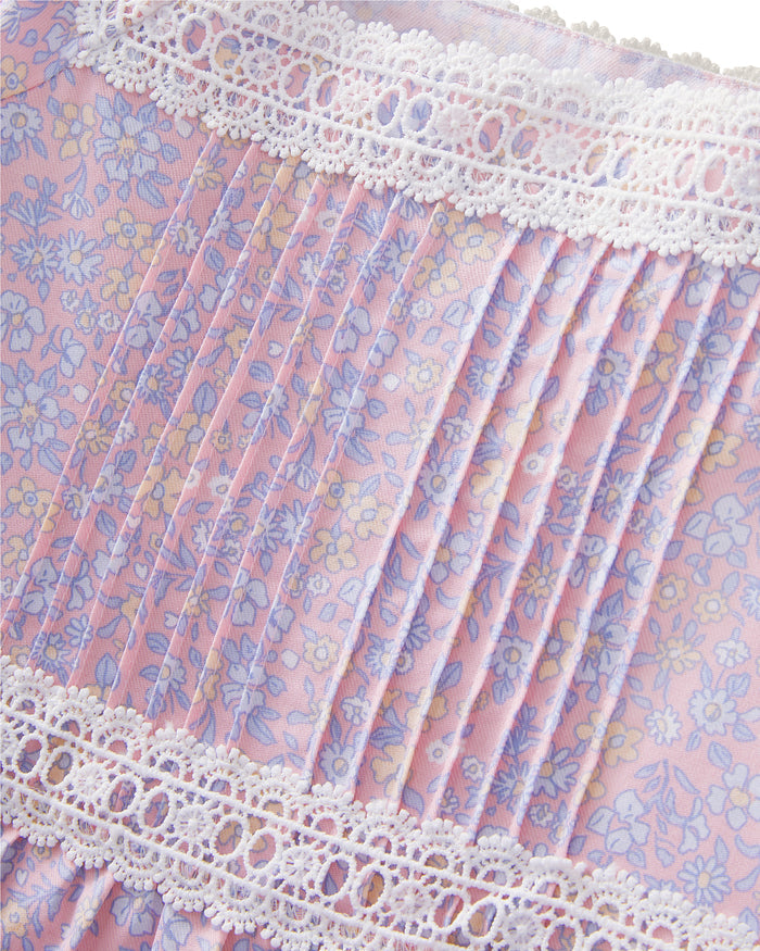 A young girl with long dark hair stands barefoot, wearing the Girl's Twill Juliette Nightgown in Fleur Blush—a light purple, knee-length dress featuring short sleeves, lace trim, and a delicate floral pattern—against a plain light background.