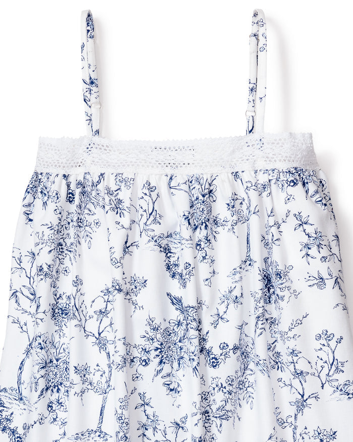 The Girls Twill Lily Nightgown in Timeless Toile by Petite Plume is a white sleeveless dress with thin straps, showcasing a blue botanical pattern and textured smocking at the neckline. It features hand-drawn flowers and leaves, perfect for those who appreciate fine craftsmanship.
